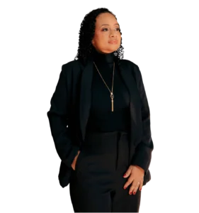 Retrato de uma mulher negra profissional (Dra. Lívia Dias), com cabelos cacheados e expressão confiante, olhando levemente para o lado. Ela veste um blazer preto, blusa de gola alta e um colar dourado, com uma das mãos no bolso e a outra sobre a calça social. Fundo branco neutro.