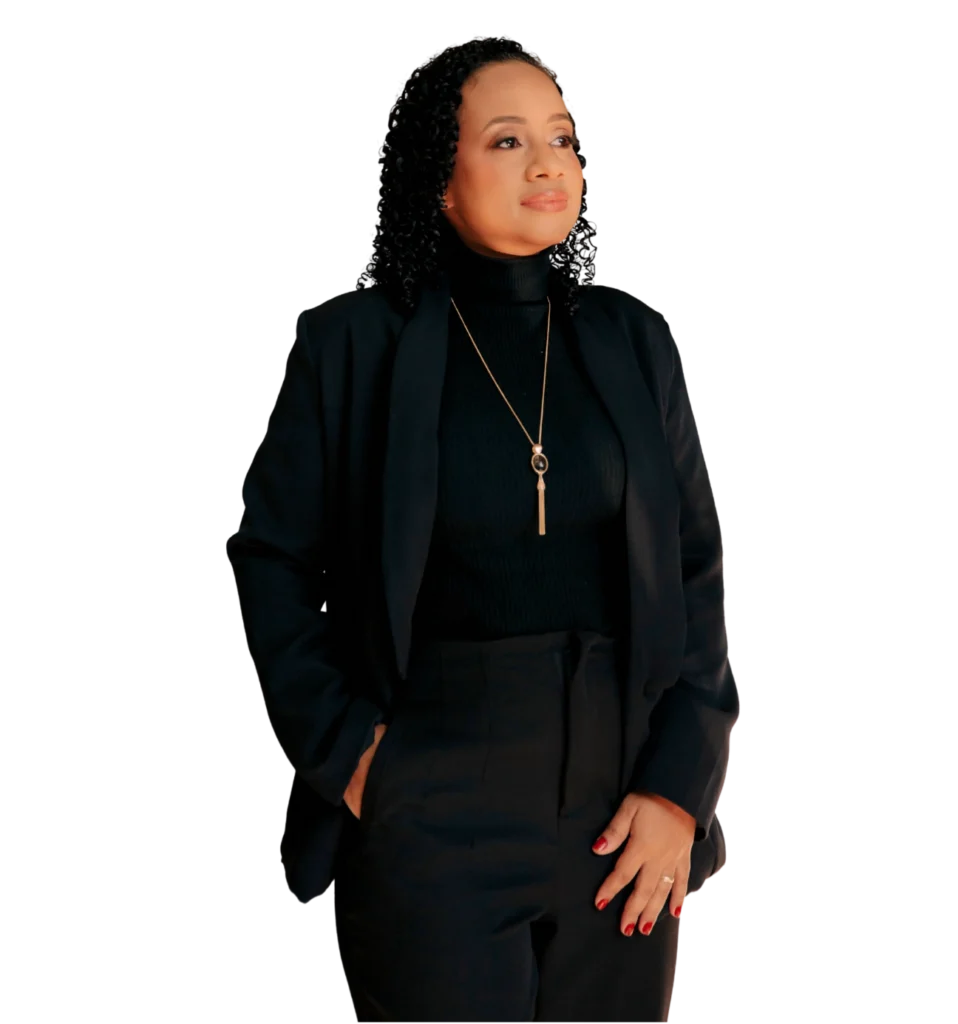 Retrato de uma mulher negra profissional (Dra. Lívia Dias), com cabelos cacheados e expressão confiante, olhando levemente para o lado. Ela veste um blazer preto, blusa de gola alta e um colar dourado, com uma das mãos no bolso e a outra sobre a calça social. Fundo branco neutro.